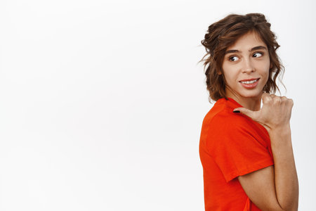 Portrait of young smiling woman pointing behind her shoulder, left at copy space, showing logo, store advertisement, promo text or banner, white backgroundの写真素材