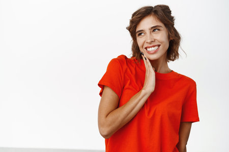 Portrait of coquettish young woman gasping, hear gossip or rumour, standing in red tshirt over white backgroundの写真素材