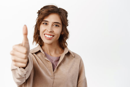 Very good. Smiling brunette girl student, hispanic woman showing thumbs up, approve like gesture, recommending, standing over white backgroundの写真素材