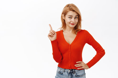Image of cunning redhead woman shaking one finger and smiling devious, saying no, rejecting, prohibit something, standing over white backgroundの写真素材