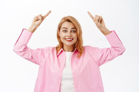 Happy young woman pointing up, showing advertisement, standing over white backgroundの写真素材