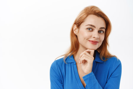 Close up portrait of smiling woman, young professional, hold hand on chin and looking confident and happy at camera, standing over white backgroundの写真素材
