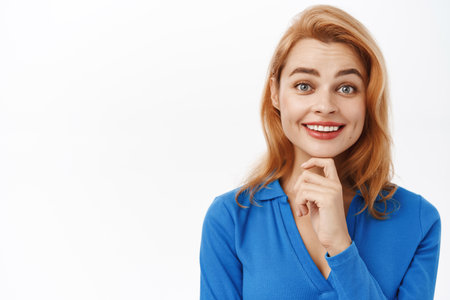 Portrait of young smiling woman listetning with interest, looking intrigued by you, standing over white background in blue blouseの写真素材