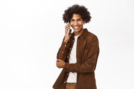 Portrait of hispanic guy talking on mobile phone, chatting or calling, standing over white studio backgroundの写真素材