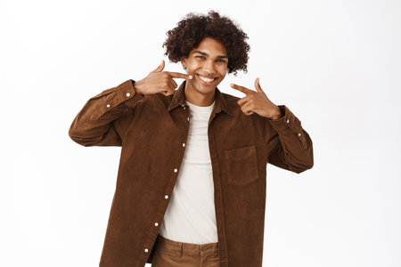 Dental concept. Portrait of smiling happy guy pointing at his healthy white teeth, standing over white backgroundの写真素材