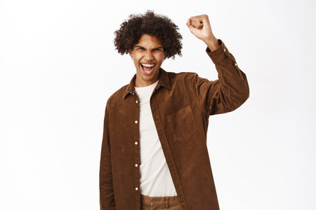 Cheerful young guy, 20 years old, raising fist, staying united, protesting or chanting, standing over white backgroundの写真素材