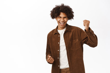 Happy guy triumphing and celebrating, saying yes with ecstatic face emotion, standing over white backgroundの写真素材