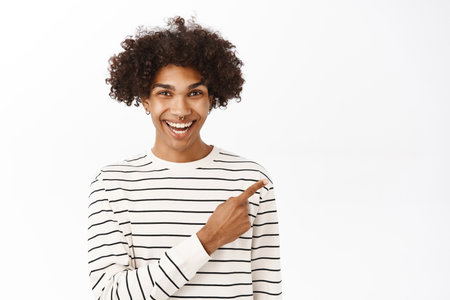 Close up portrait of young hispanic guy pointing finger right, showing advertisement, promo offer, announcement banner aside, standing over white backgroundの写真素材