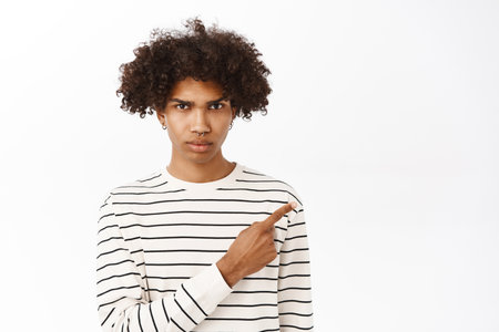 Close up portrait of concerned young man with curly hair, pointing finger right, showing smth alarming, standing over white backgroundの写真素材