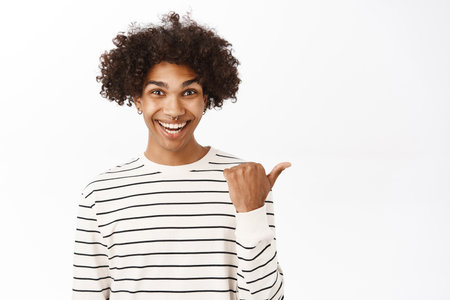Close up portrait of young hispanic guy pointing finger right, showing advertisement, promo offer, announcement banner aside, standing over white backgroundの写真素材