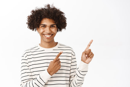 Close up portrait of smiling handsome man, pointing fingers right, showing advertisement, banner, standing in casual clothes over white backgroundの写真素材