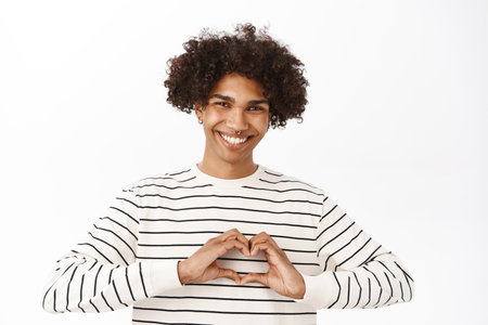 Close up portrait of smiling handsome guy, showing heart, love gesture and looking happy, standing over white backgroundの写真素材