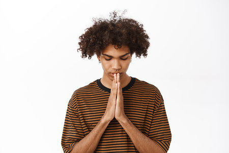 Close up of young hopeful guy, boy praying with hope, standing over white studio backgroundの写真素材