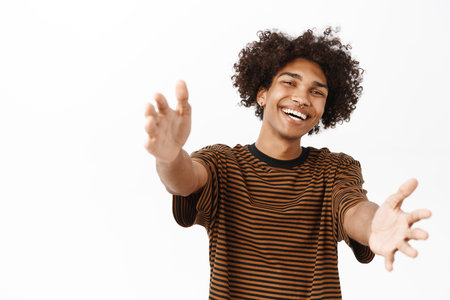 Happy smiling guy stretching out arms towards you, hugging, receiving in his hands, standing over white studio backgroundの写真素材