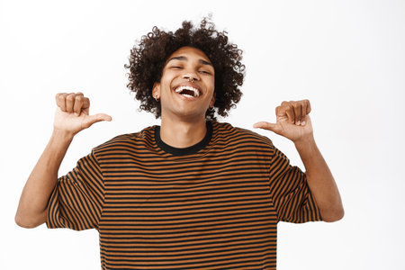 Confident young hispanic man pointing at himself with proud, satisfied smiling face, standing over white studio background, looking coolの写真素材