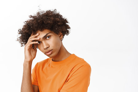Close up portrait of handsome boy, queer guy with curly hair, looking like model at camera, standing over white studio backgroundの写真素材