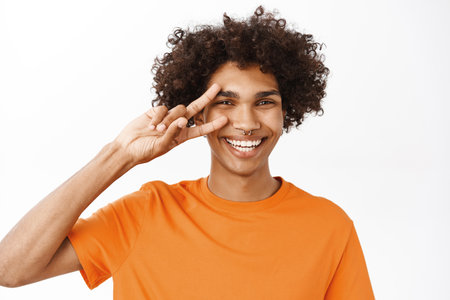 Close up portrait of smiling hispanic man showing peace, v-sign near eyes and looking happy, positive people and emotions, standing over white backgroundの写真素材