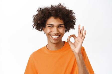 Alright. Smiling hispanic man showing okay, ok sign in approval, recommending, like smth good, standing over white backgroundの写真素材