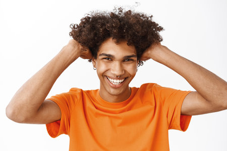 Close up of handsome hispanic boy, guy showing his curly healthy, natural hair, touching haircut and smiling, standing over white backgroundの写真素材
