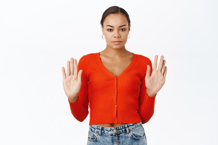 Serious young black woman showing stop gesture, raising palms hands up, prohibit something, rejecting, standing over white backgroundの写真素材