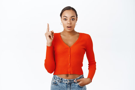 Portrait of surprised latina woman, pointing finger up, looking amazed, standing over white backgroundの写真素材