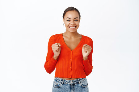 Portrait of excited woman winning, celebrating, jumping from excitement and happiness, triumphing, standing over white backgroundの写真素材