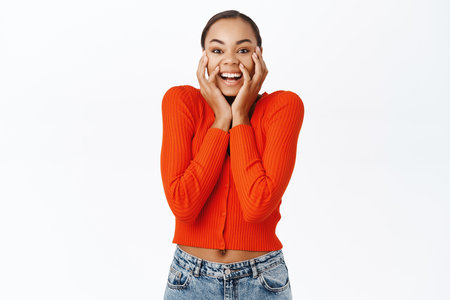 Image of excited young woman looking surprised, amazed by great news, standing over white backgroundの写真素材