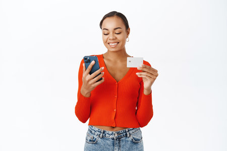 Technology and online shopping. Smiling woman using mobile phone and credit card, standing happy over white background, ordering smthの写真素材