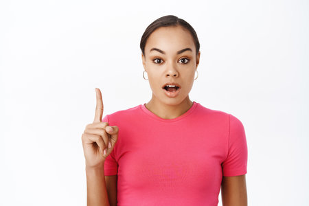 Close up of surprised woman, pointing finger up, gasping and saying wow, showing promo offer, impressed by banner advertisement, white backgroundの写真素材