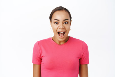 Close up of enthusiastic young woman, looking surprised and amazed, impressed reaction, standing over white backgroundの写真素材