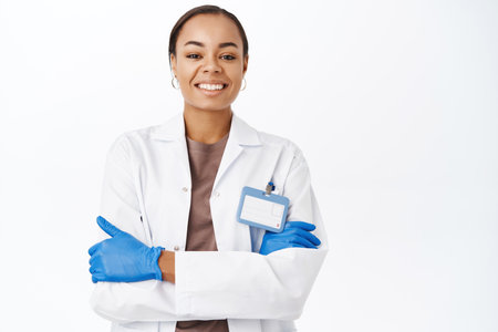Confident medical doctor in gloves, cross arms on chest, standing over white studio backgroundの写真素材