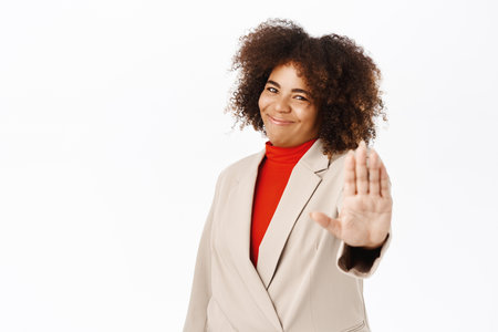 Please no. Smiling african american saleswoman, corporate woman shows stop sign, extends palm to prohibit smth, stands over white backgroundの写真素材
