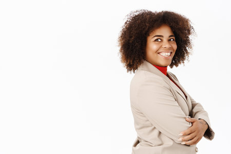Portrait of smiling african american businesswoman, company worker in suit, standing half turned, looking professional, standing over white backgroundの写真素材