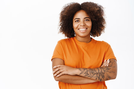 Portrait of modern smiling woman with tattoos, wears orange t-shirt, looks happy, stands over white backgroundの写真素材