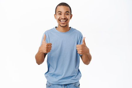 Smiling arab man shows thumbs up, recommends, gives positive feedback and his approval, stands over white backgroundの写真素材