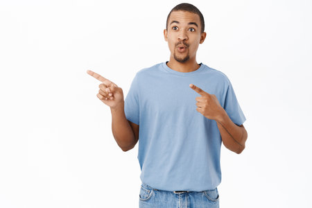 Surprised arab guy pointing left, shows direction, say wow, impressed by advertisement, stands over white backgroundの写真素材