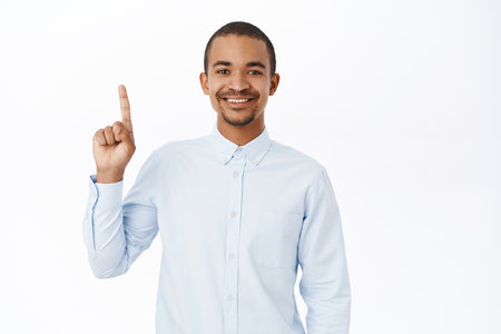 Handsome smiling arab man pointing up, showing advertisement, company banner or logo, standing in blue shirt over white backgroundの写真素材