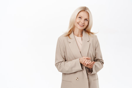Smiling senior woman, older lady in her 50s, wearing trench coat, streeth clothing, standing over white backgroundの写真素材