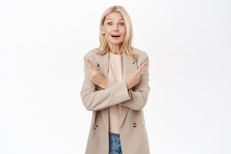 Portrait of elegant mature woman, lady pointing sideways left and right, looking amazed with variants, lots of opportunities, standing over white backgroundの写真素材