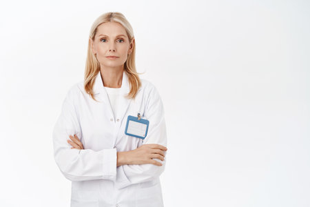 Smiling mature dermatologist, female docor, looking confident, ready to help patients, stands over white backgroundの写真素材