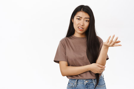 Confused korean girl looks puzzled, shrugs shoulders and looking clueless, stands in tshirt over white studio backgroundの写真素材