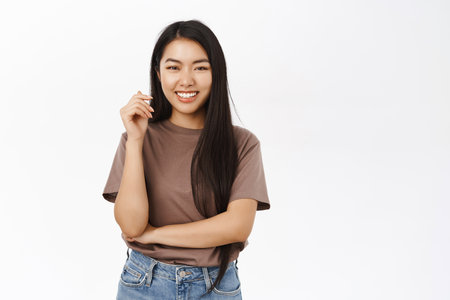 Portrait of beautiful laughing asian girl looking positive, happy face expression, relaxed pose, standing in brown tshirt over white backgroundの写真素材
