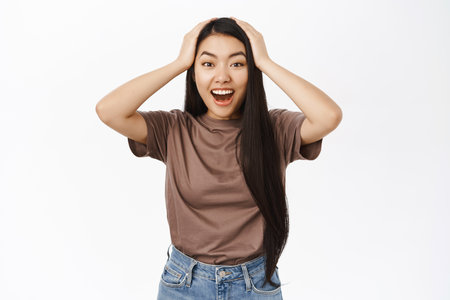Portrait of asian girl looks surprised, amazed by awesome news, gasping, looking fascinated, white backgroundの写真素材