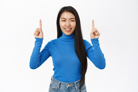 Portrait of stylish korean girl points up, smiles and looks excited, shows banner, advertisement, stands over white backgroundの写真素材