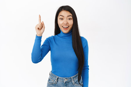 Portrait of stylish korean girl points up, smiles and looks excited, shows banner, advertisement, stands over white backgroundの写真素材