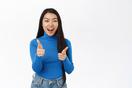 Portrait of enthusiastic beautiful female model, pointing fingers at herself and smiling, choosing, inviting you, congratulating, white backgroundの写真素材