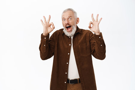 Super good. Impressed funny old guy, senior man showing okay sign, approval, standing over white background with ok gestureの写真素材