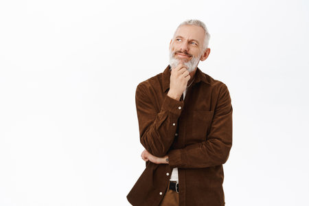 Thoughtful senior man, looking aside and planning, thinking of something, standing against white background in casual clothesの写真素材