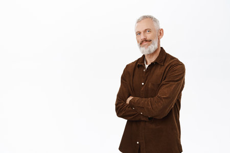 Image of happy old guy with white hair and beard, cross arms on chest, smiling and looking pleased at camera, standing in casual clothes over white backgroundの写真素材