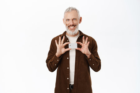 Mature man with grey hair smiling, showing credit card, senior guy recommending bank, standing over white backgroundの写真素材